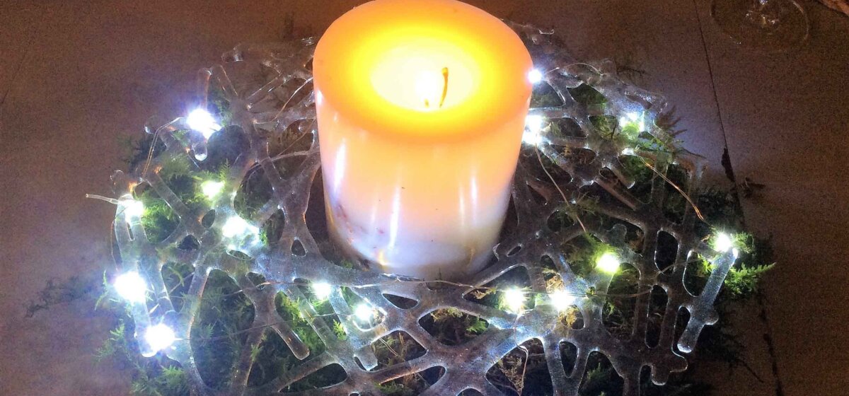 A candle surrounded at its base by a lattice glass wreath with entwined fairy lights.