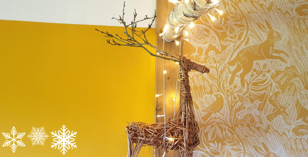 An image of a reindeer made from willow sticks against a yellow background with fairy lights and snowflakes in the corners.