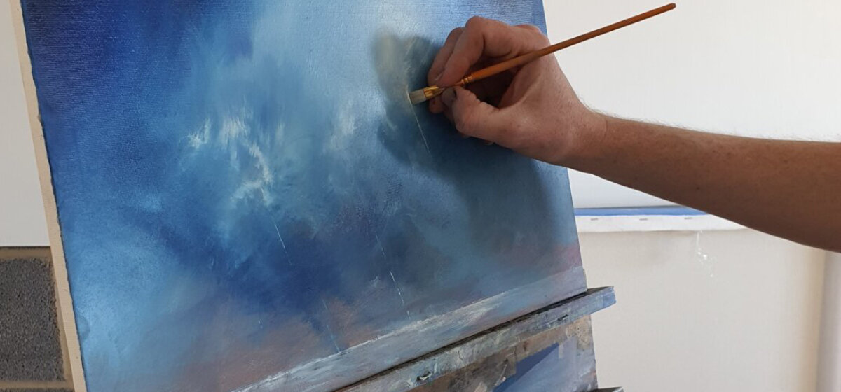A blue oil painting on a canvas with someone hand painting with a paint brush