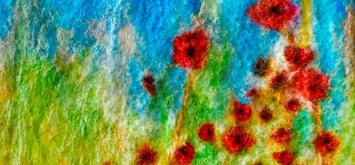 A close up image of a felt image of green grass with blue sky and red poppies.
