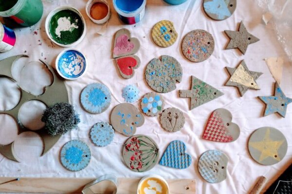 An image for Festive Clay Decoration Making at The Base, Greenham, pictured is various shapes cut out of clay surrounded by paints to decorate them