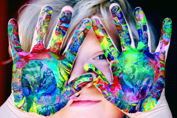A child holds their multi-coloured paint hands over their face