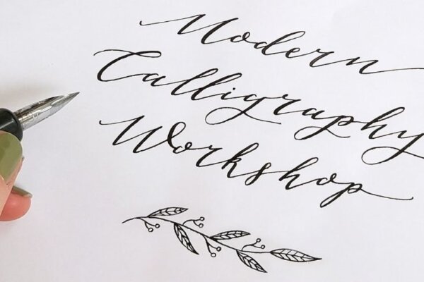 Image of a hand holding a fountain pen to a page which has text that reads: Modern Calligraphy Workshop in a cursive font. Underneath is a small vine drawing.