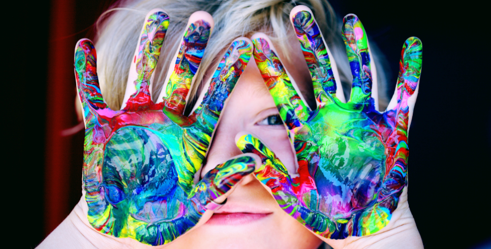 A child holds their multi-coloured paint hands over their face