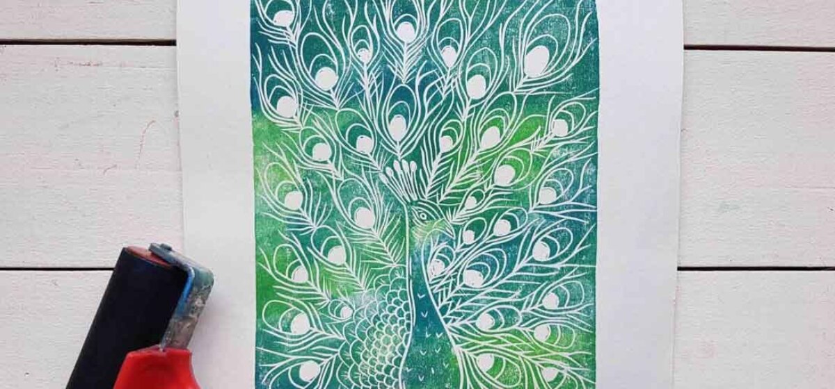 A beautiful green and blue print of a peacock sits next to a linoprint roller