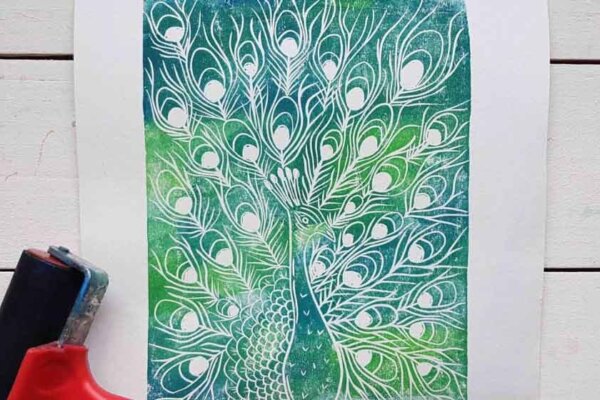 A beautiful green and blue print of a peacock sits next to a linoprint roller