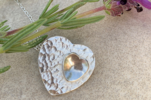 A beautiful silver heart pendant sits on display next to a sprig of lavender