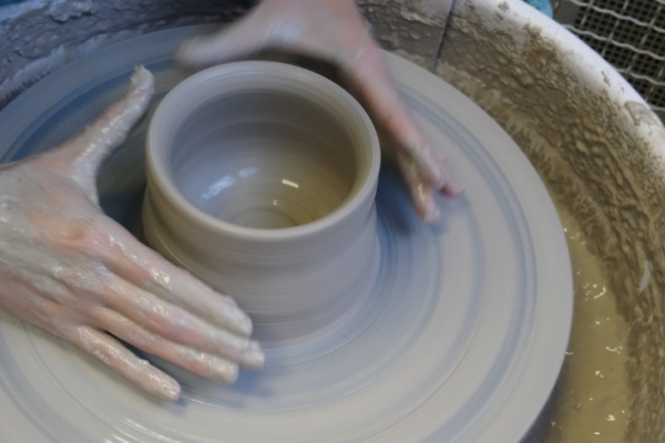 A pottery wheel spinning with a person shaping a pot with their hands