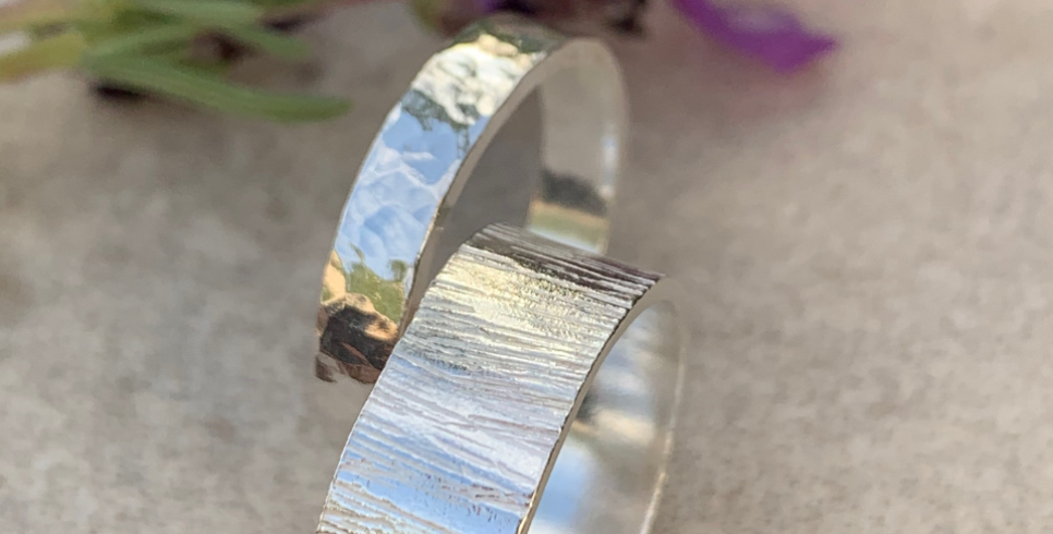 Two silver band rings stand on their sides together, one thing band and one thick