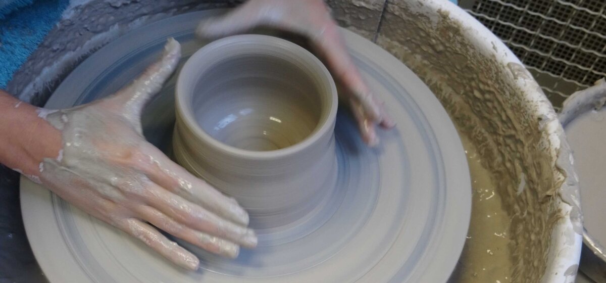 A pair of hands is forming clay into a bowl on a potters' wheel.