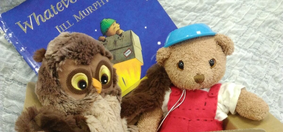 A photo of a book with two stuffed animals, one of an owl (left) and one of a bear (right) on top.