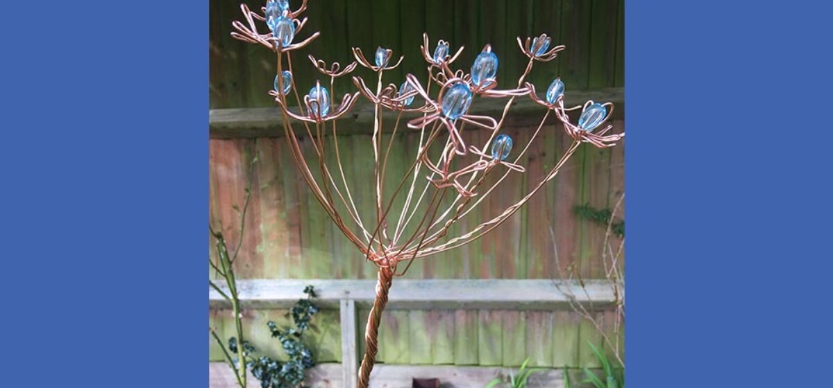 A close up of a wire flower garden sculpture, with blue beads at the center of each flower head.