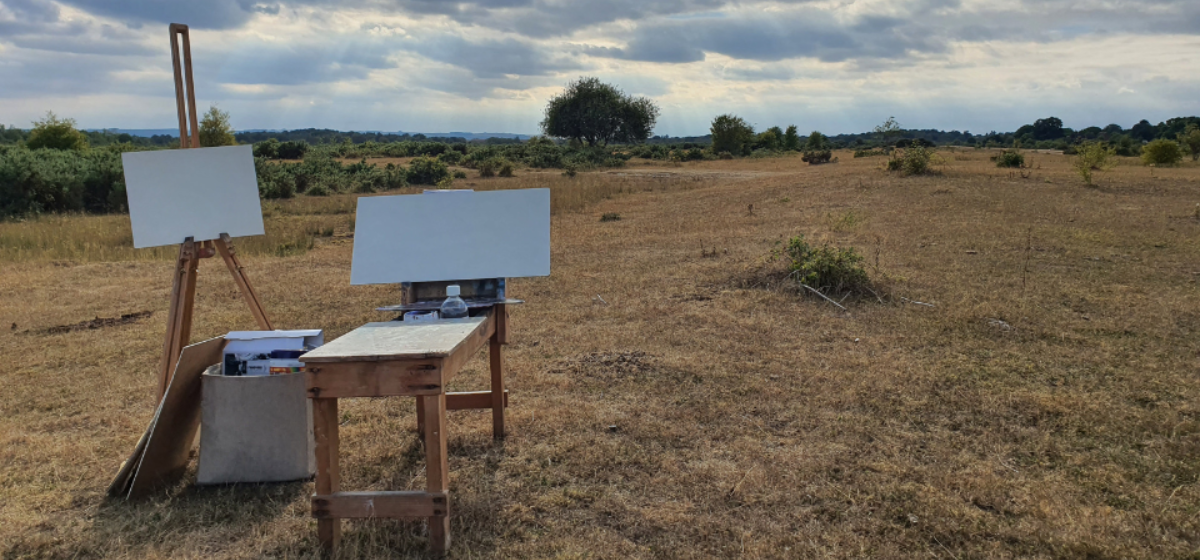 This is photo of a field and on the left hand side there are two empty canvases set up alongside a wooden table.