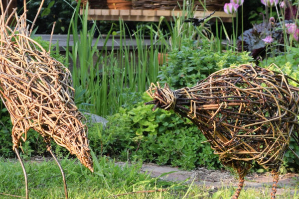 A photo of two chickens made from willow in a green garden.