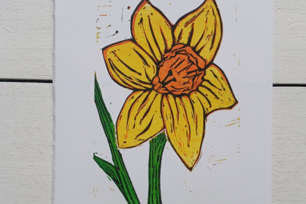 Lino printed Daffodil in yellow, orange and green with a sold black outline on a white background