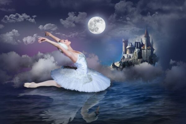 An image from Swan Lake coming to the Corn Exchange Newbury, a ballerina leaps across the image in a white tutu lit by the moonlight behind her