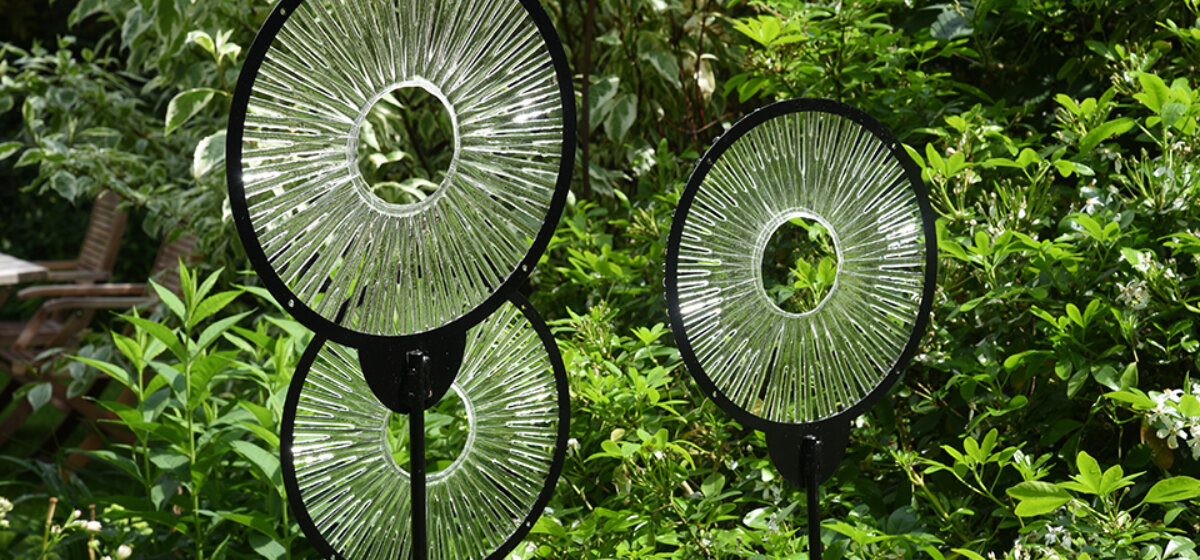 Three glass circular sculptures in a garden.