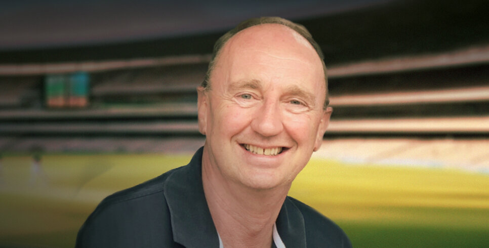 An image of cricket commentator Jonathan Agnew smiling a the camera with a cricket pitch blurred in the background.
