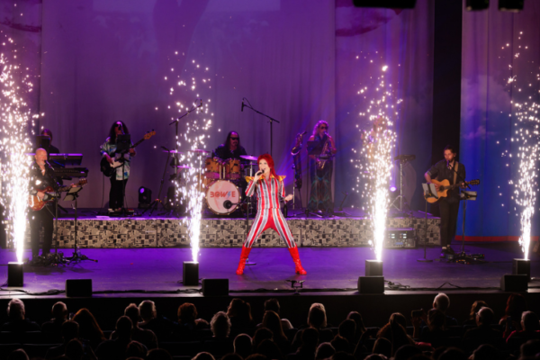 A Bowie tribute act dressed in a silver and red stripy jumpsuit in front of a stage with sparklers