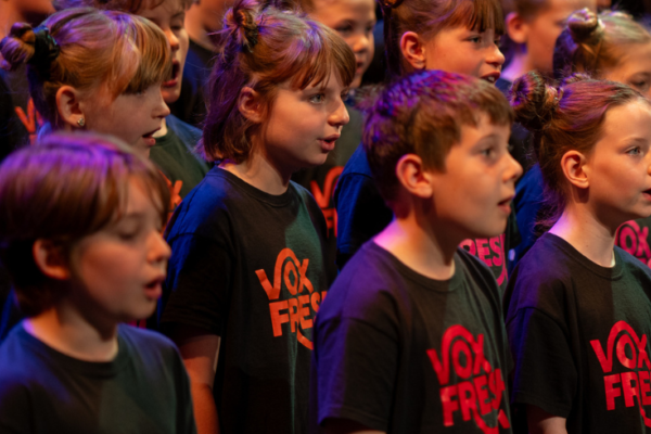 A group of children sing together, wearing black t-shirts with red text saying VoxFresh