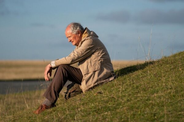 A still of an old man sat on a grassy hill looking out.