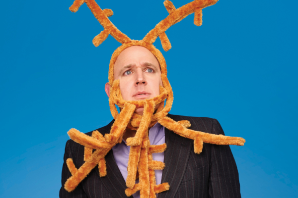 A bald man wearing a suit looks puzzled as he sports several antlers on his head
