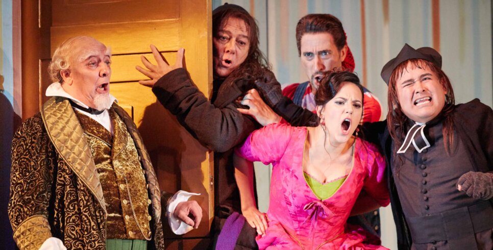 five people on stage, one behind a door, all with open mouth expressions on face