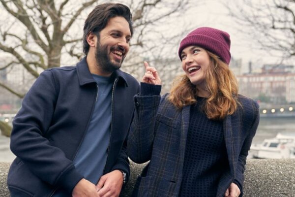 A photo of actor Shazad Latif on the left and actress Lily James on the right. They are both smiling and she is pointing a playful finger at him.
