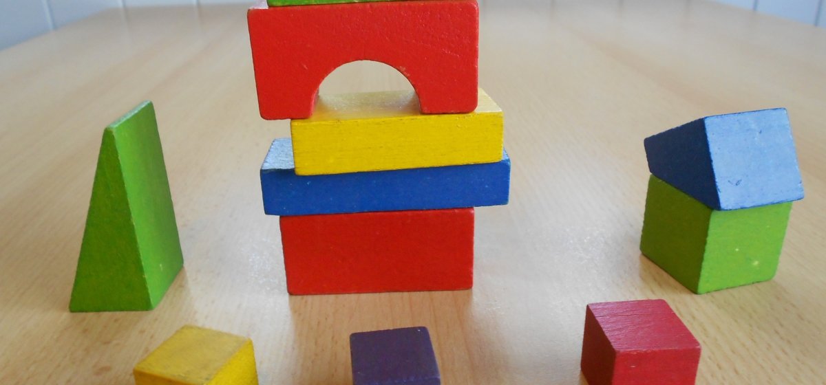 A selection of wooden blocks of different colours and shapes. In the middle is a stack of blocks with a scatter of singular blocks around it.