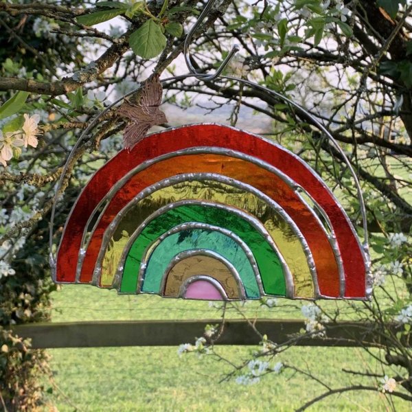 A rainbow glass hanging from a tree with a green rural landscape in the background