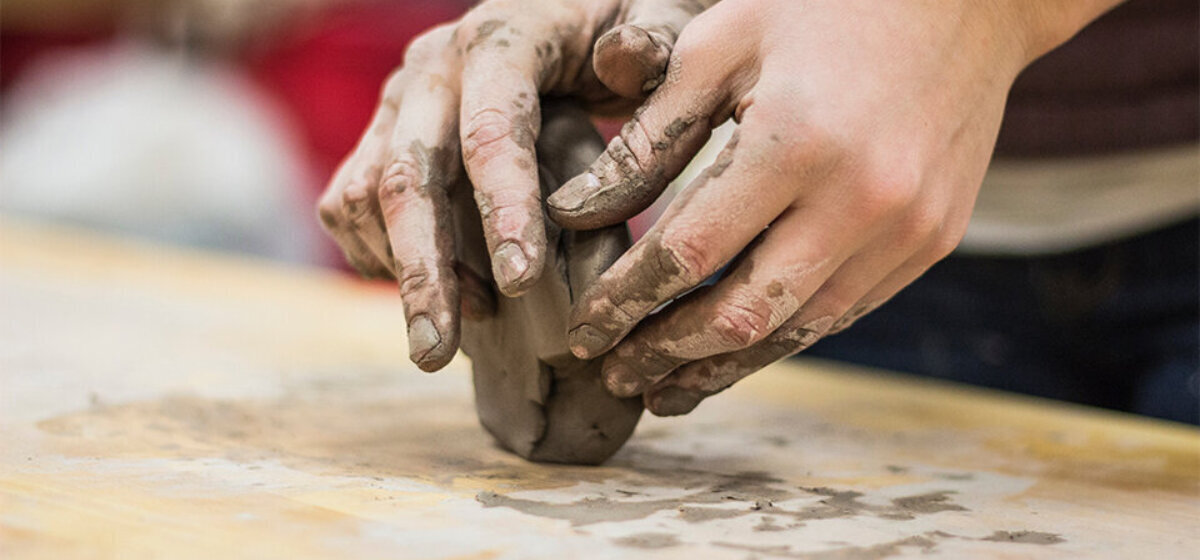 An image of two hands moulding some clay on a table.