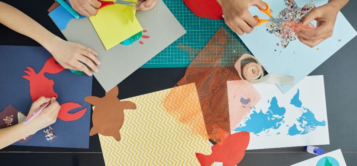 A overhead view of hands cutting out and sticking scraps of paper in various animal shapes.