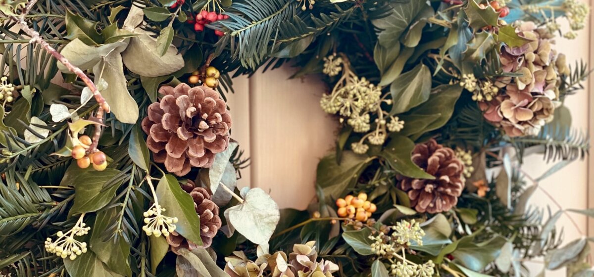 A wreath made with flowers and foliage hanging on a door.