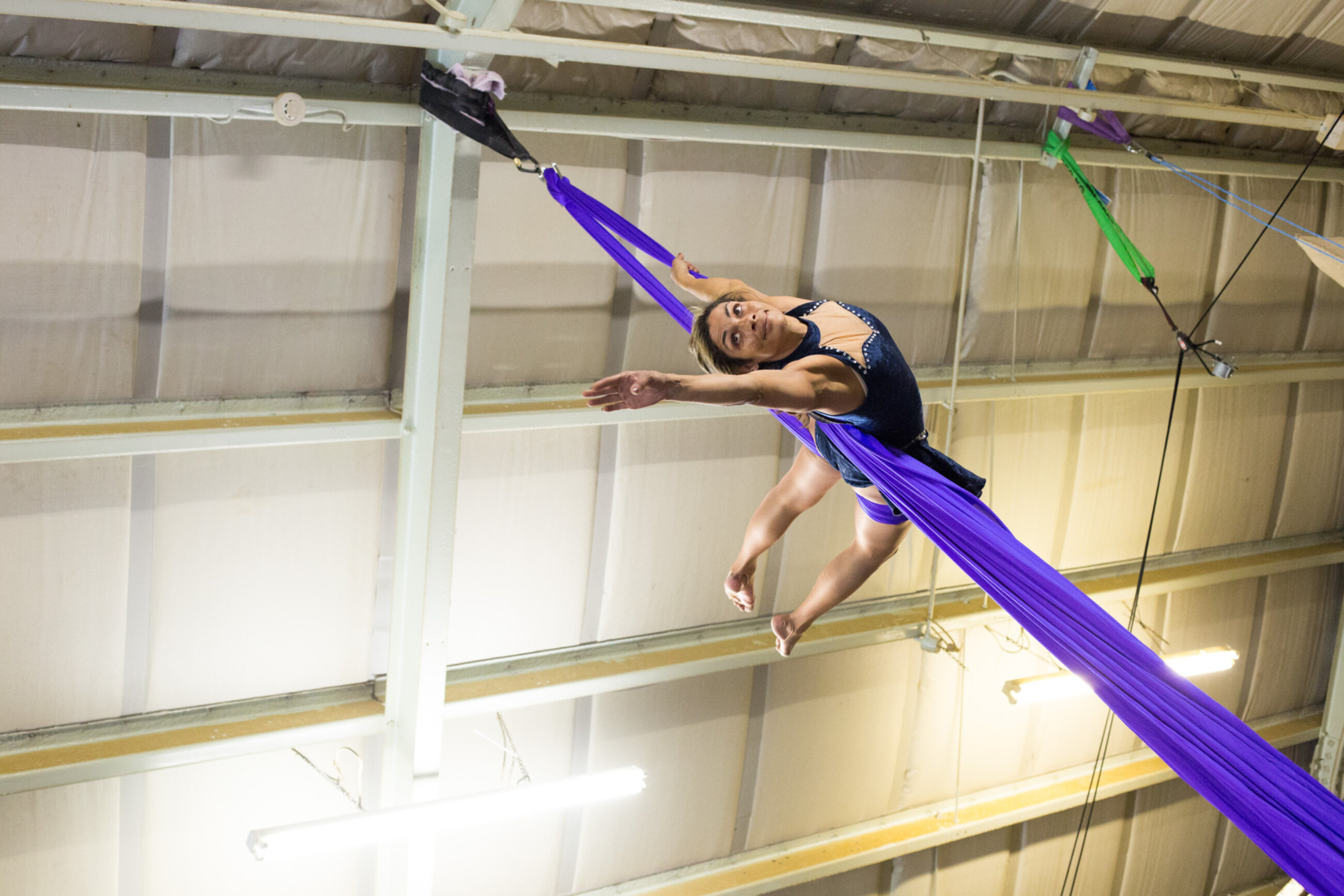 Aerial artist training on aerial silks holding a crescent pose with body. Image taken from ground looking up.