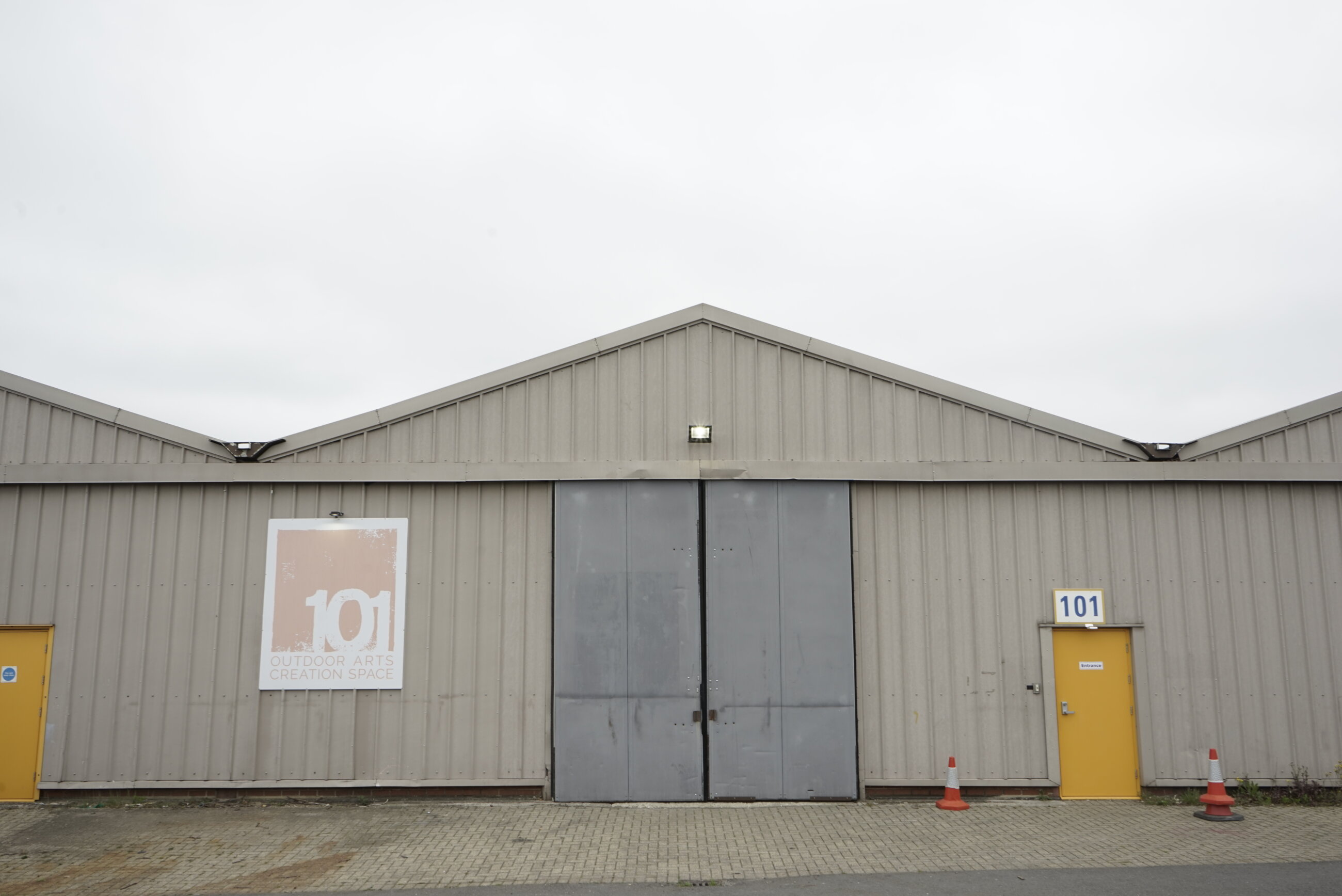 Front facade of 101 building. A grey warehouse with a pitched roof and orange doors and 101 sign