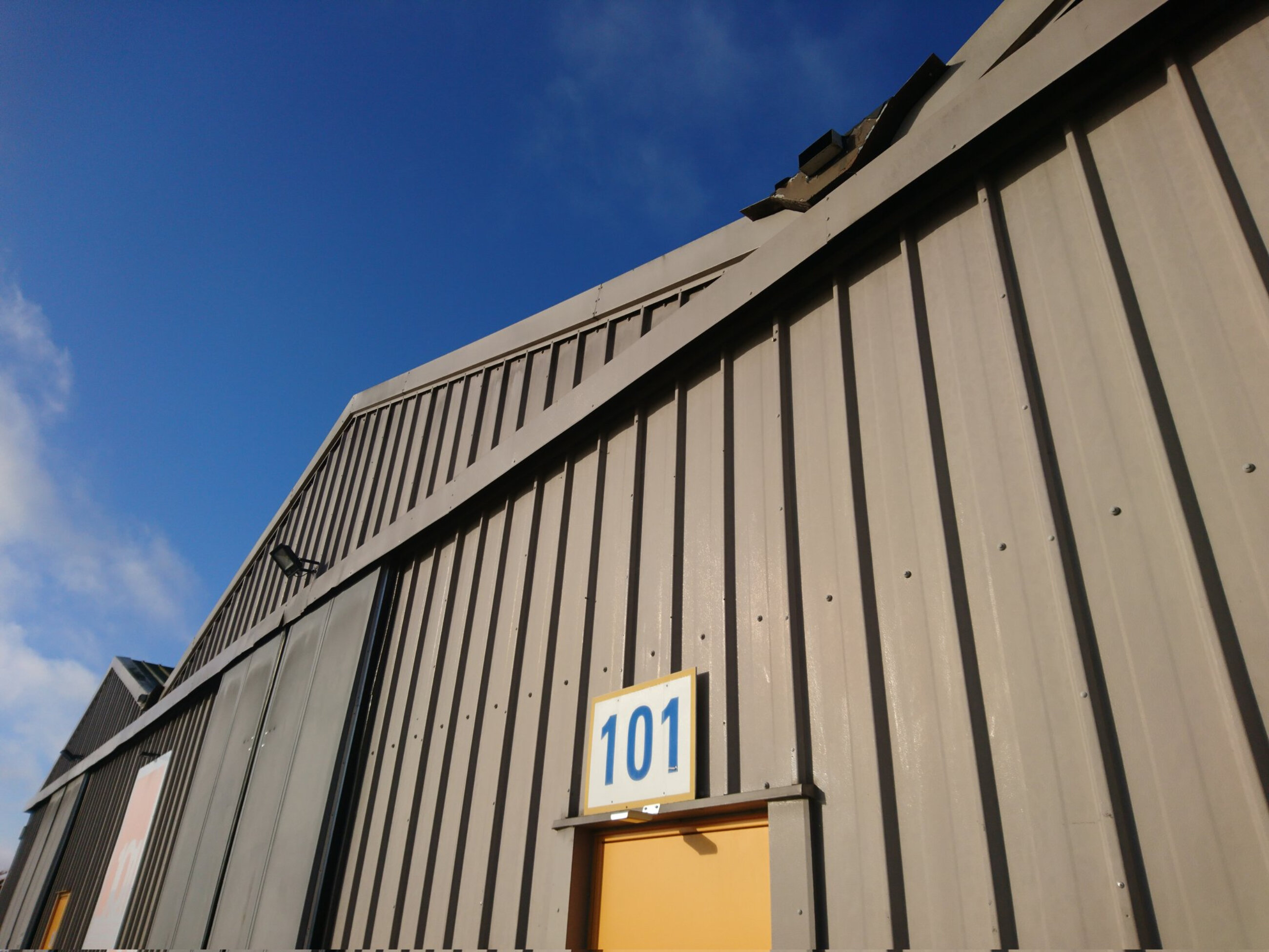 Facade of 101 facility, a grey warehouse with an orange door and 101 sign above the entrance