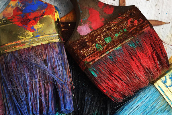 a close up of wide paintbrushes with paint. There are red, purple and blue colours