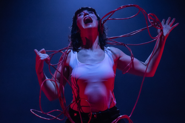 A woman on stage with red wire wrapped around her on a blue stage