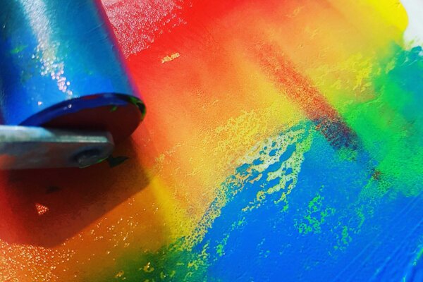 An image of coloured paint in rainbow colours with a roller in the top left hand corner.