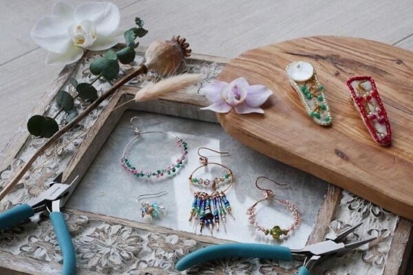 A photo of a decorated photo frame on which pliers, flowers and beaded jewellery lay. There is also a wooden board on the frame which have two beaded hairclips and a flower
