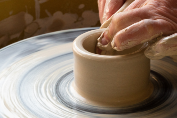 Clay on spinning table being shaped by hands into pot