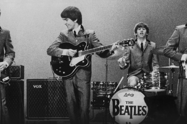 A black and white image of The Beatles all dressed in suits, performing on stage