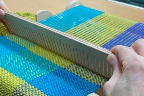 Blue and green wool on a weaving loom with hands.
