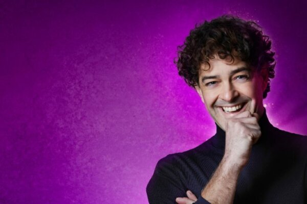 Lee Mead stands smiling against a purple background