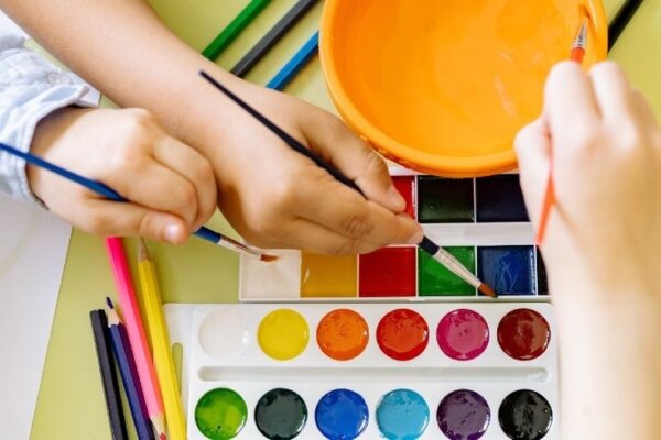 Children's hands with paintbrushes and colourful paints.