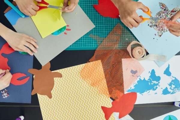 A overhead view of hands cutting out and sticking scraps of paper in various animal shapes.