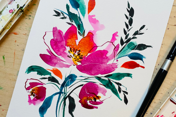 A pink watercolour flower on paper surrounded by a paint palette and brush