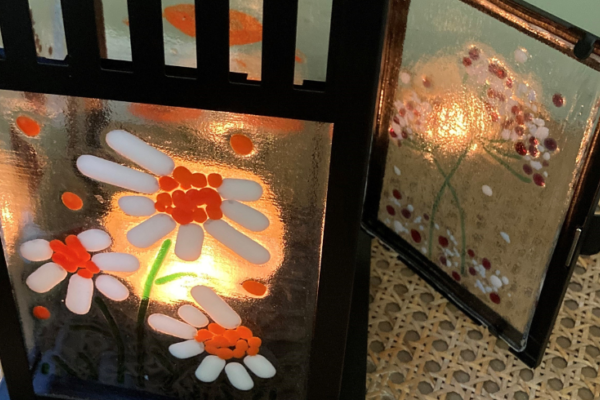 A candle-lit glass lantern with a floral orange pattern