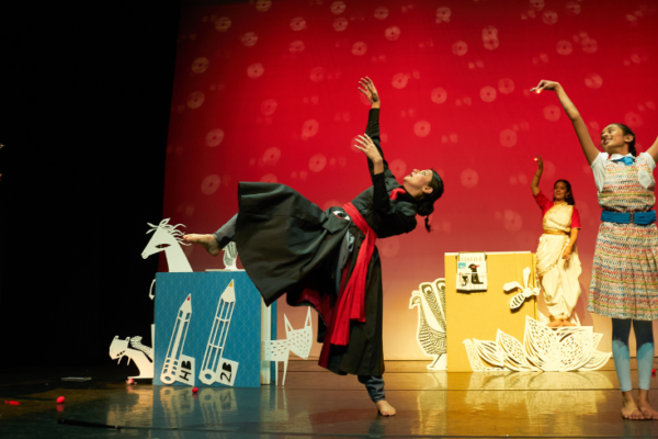 Three women dancing on a red stage surrounded by paper cuts