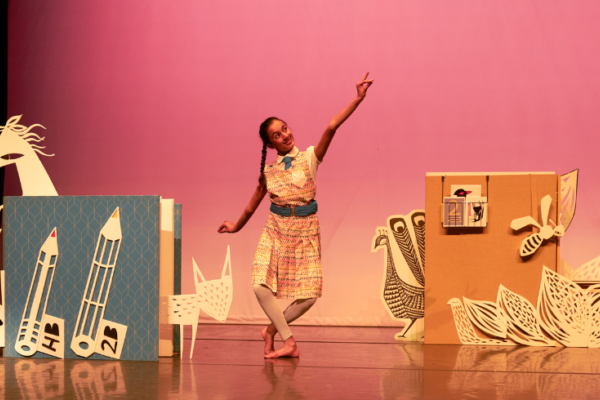 A girl on a pink stage surrounded by paper cuts